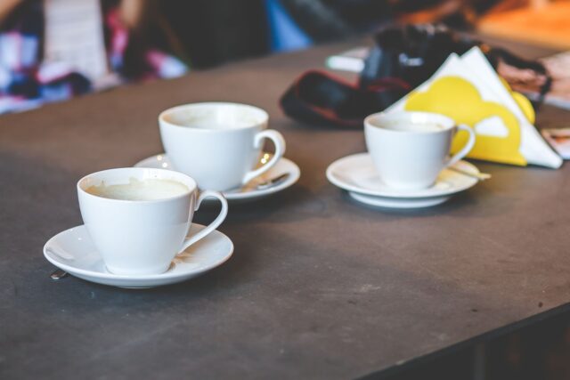 Mai multe cești de cafea goale pe o masă de lemn, sugerând un consum mare de cafea pe parcursul zilei